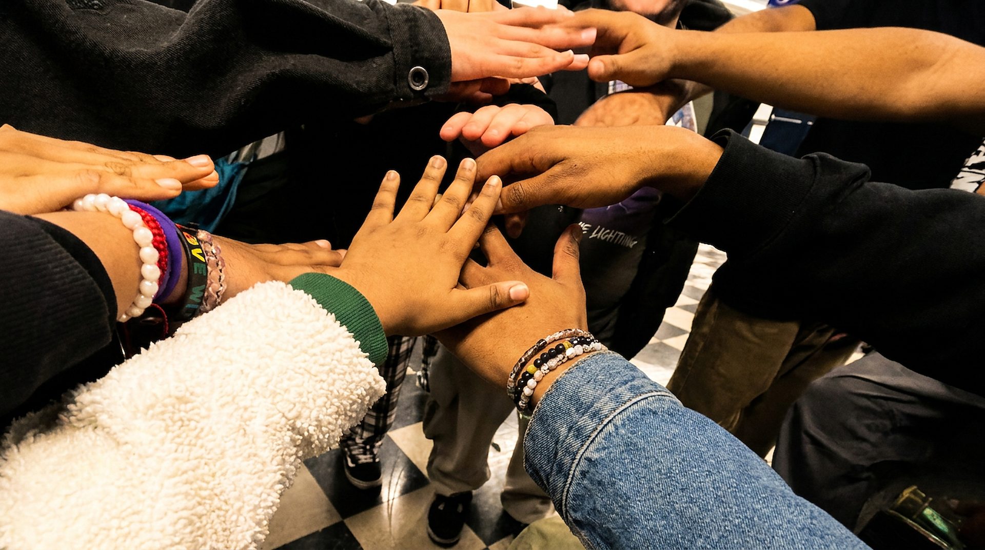 A dozen hands, youth and adults together, stacked in the middle of a huddle at the end of a session.